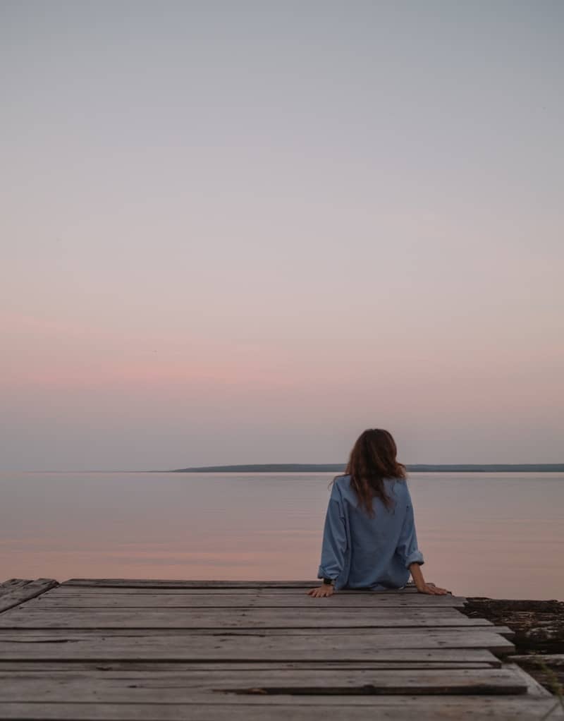 Woman sitting on wooden dock overlooking calm water