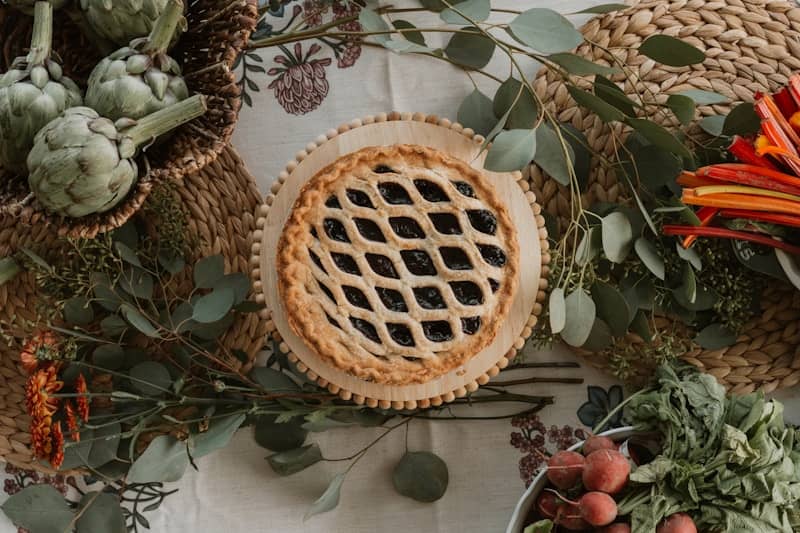 A lattice-top pie surrounded by autumn harvest vegetables and greenery.