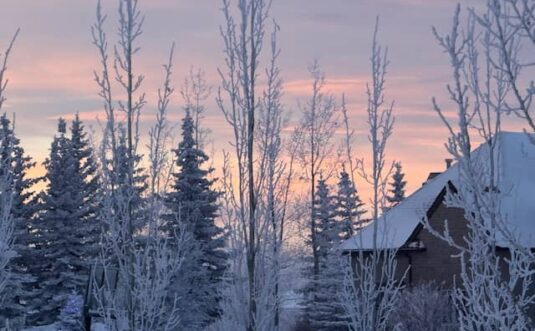 A cabin in a snowy picture at sunset