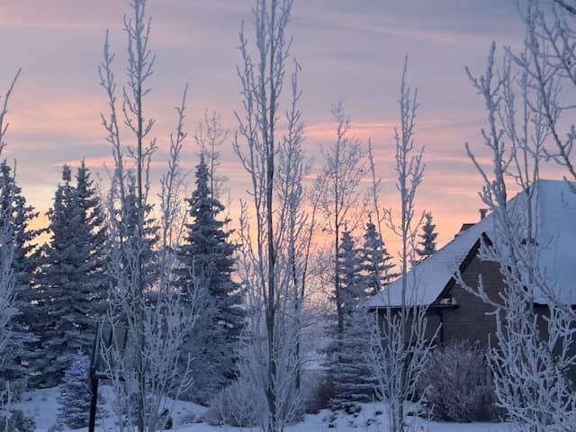 A snowy cabin in the woods at sunset