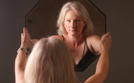 A woman standing in front of a mirror brushing her hair